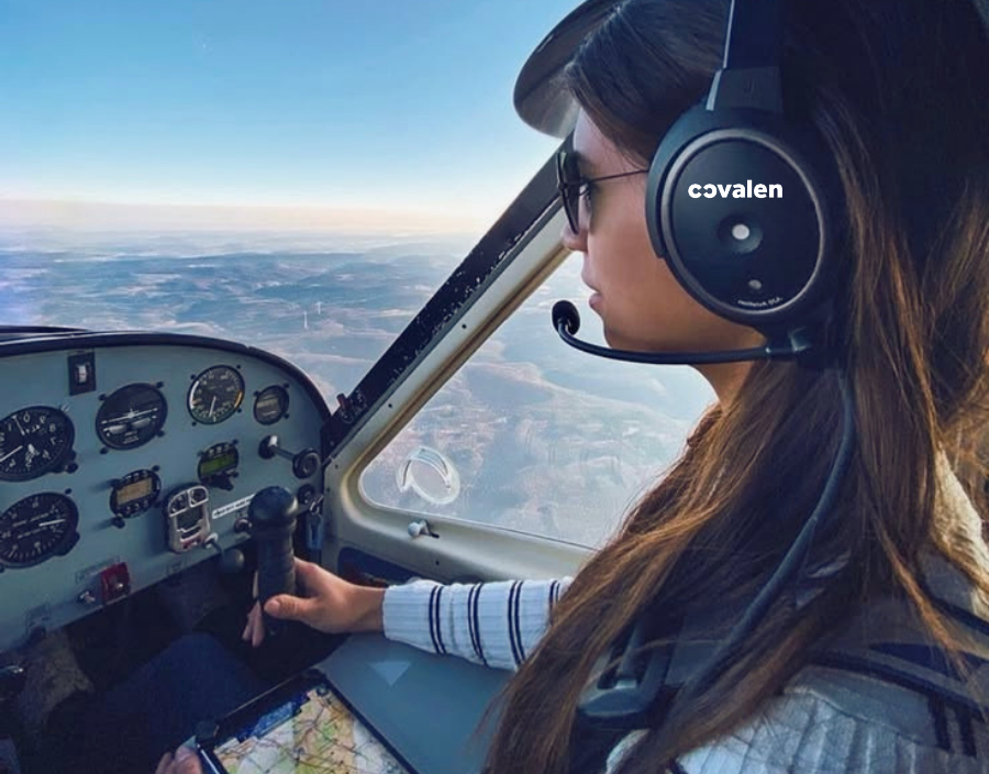 Female pilot wearing an aviator headset and sunglasses, flying a small aircraft, cockpit view with sky and horizon in the backround